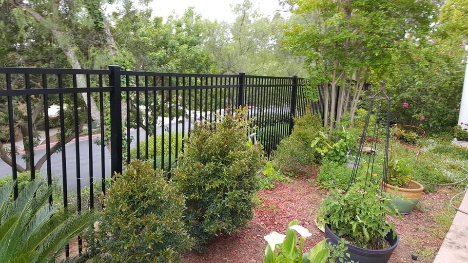 Black iron fence beside a landscaped planting bed with potted plants