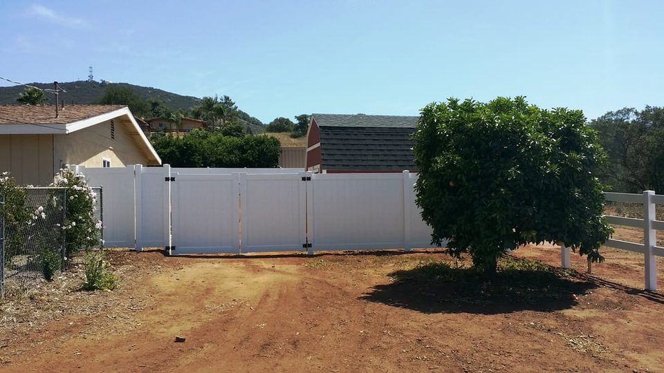 White vinyl fence on a dirt lot with rolling hills behind it