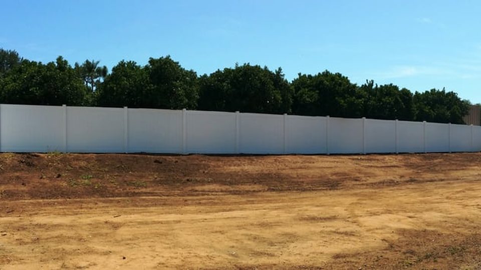 White vinyl fence running across a wide graded lot
