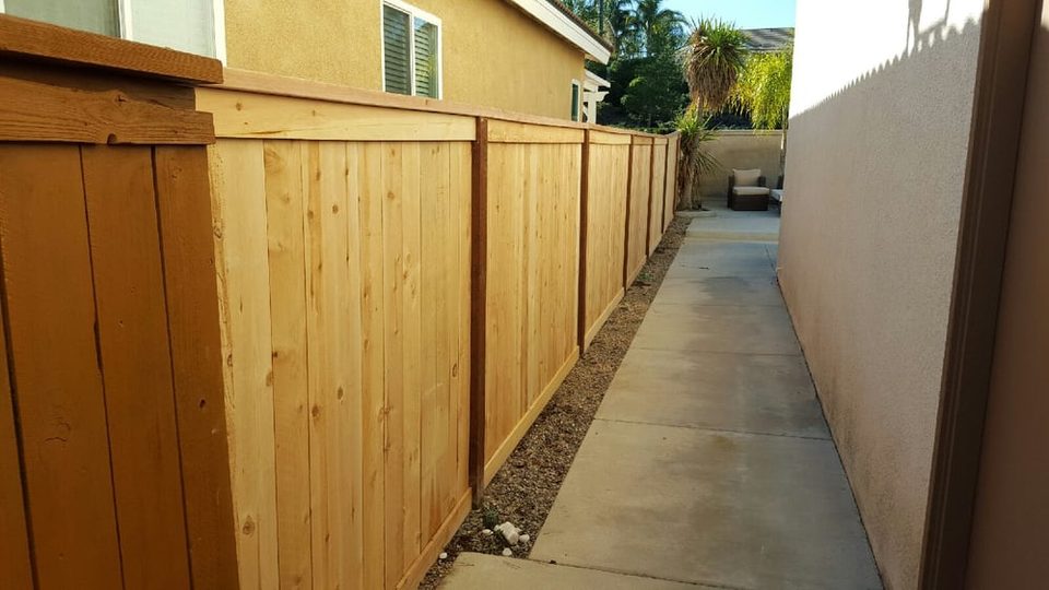 Tall wood privacy fence running along a concrete walkway